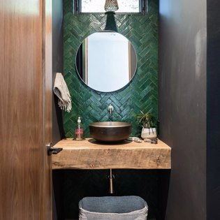 A bathroom sink with a pine green backsplash and round mirror