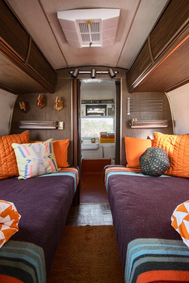 Twin beds with orange pillows and purple blankets inside the Airstream trailer.