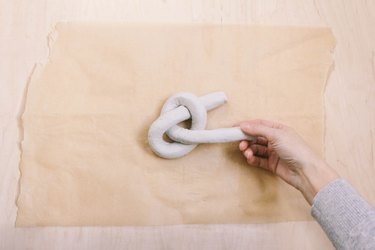 Pulling tail of air dry clay through hole to form a knot