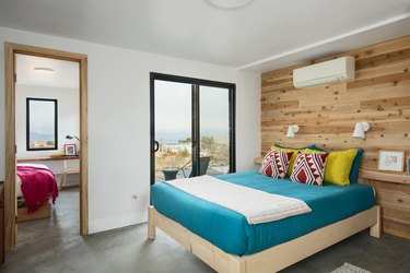 A bedroom with wood panel wall and slider door to outside.