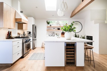 open kitchen with large island, wood floor, overhead wood beam, white lower cabinetry and wood uppers