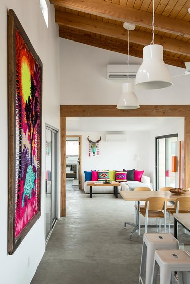 A view from the kitchen towards the living room with pendant lamps, beamed ceilings and concrete floors.