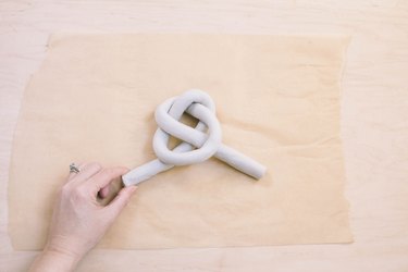 Shaping tube of air dry clay into a knot