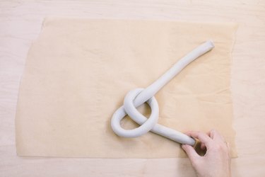 Shaping tube of air dry clay into a knot