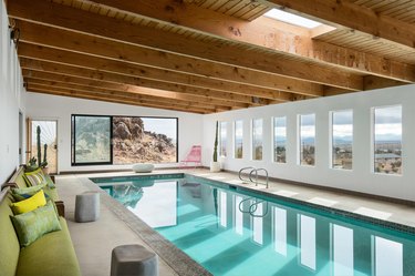 A wide shot of the indoor pool area with wood beamed ceilings, skylights, and large slider doors and windows.