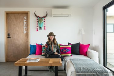 Kelly Van Patter sits on a sectional couch with colorful textile pillows in her desert home.