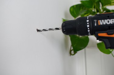 Power drill drilling through a white wall with a plant in the background