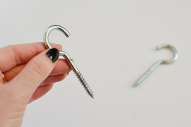 Hand holding a silver screw hook with a second screw hook in the background