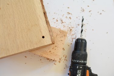 Power drill next to a piece of wood with a hole drilled through the corner