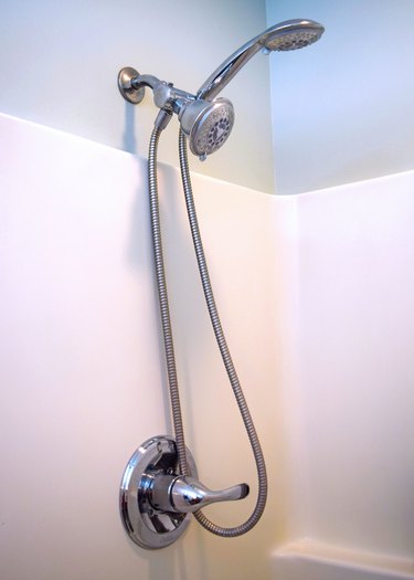 A chrome dual showerhead in a white shower with sea salt green walls. One of the heads is removable with a long hose.