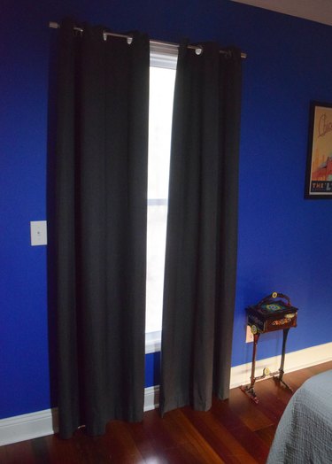 A window with two dark curtains on each side, with a wood floor and blue walls.