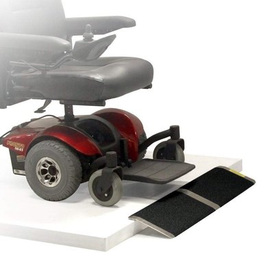 A red and black power wheelchair approaches a small black and aluminum ramp.
