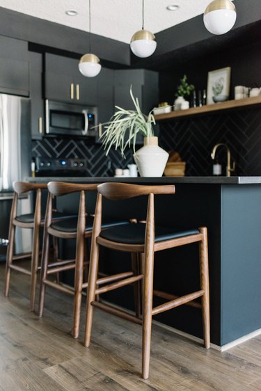Black kitchen island with seating featuring wood stools and globe-style pendant lights