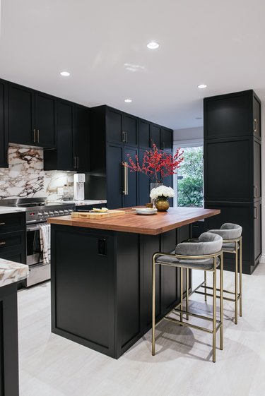 Black kitchen island with seating featuring brass bar stools and wood countertop