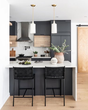 Black kitchen island with seating featuring white pendant lights and light wood finishes