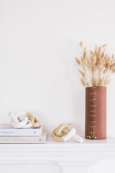 two clay knot sculptures on a mantel with books and dried flowers