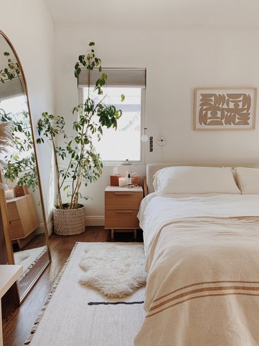 modern fall decor in neutral bedroom with bed and mirror and plant in the corner