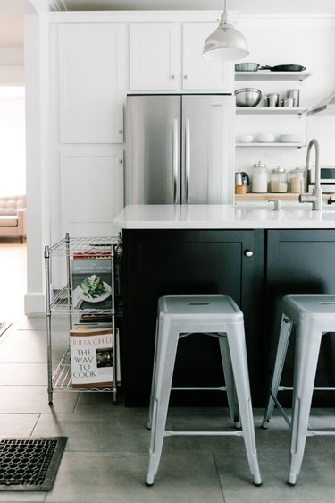 Black kitchen island with seating featuring featuring vintage metal chairs and white cabinets