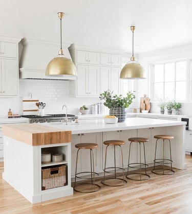 White T-shaped kitchen island with butcher block, storage cubbies, and gold pendant lights