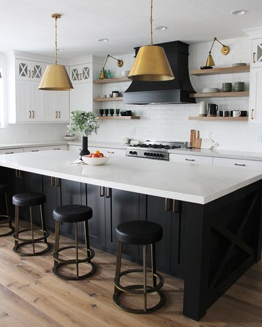 Black kitchen island with seating featuring brass bar stools and brass pendant lights