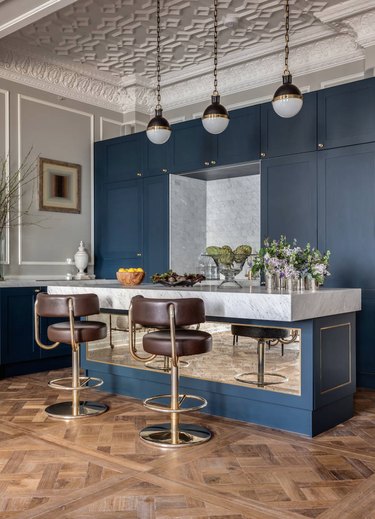 Inlaid wood floors, marble topped kitchen island, Art Deco stools and steel blue cabinets in a high ceiling kitchen.