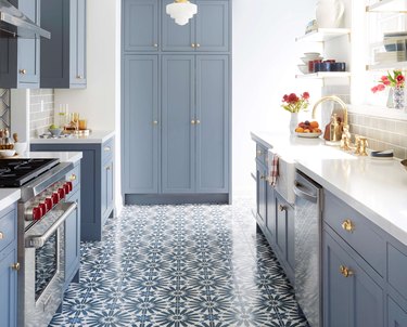 Blue patterned tile floor, blue cabinets, white counters and white pendant light.