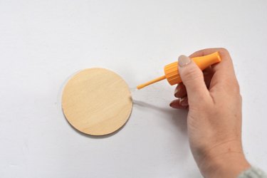 Hand holding brush with glue against wooden circle.