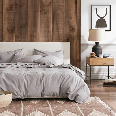 bedroom showing a bed with gray sheets and a wood backdrop with a side table and framed art print nearby