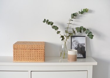 Cane box on white shelf with vase with eucalyptus