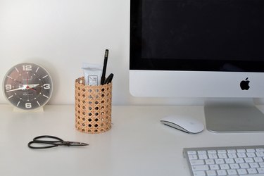 Cane pencil pot next to computer, clock, scissors and keyboard in background.