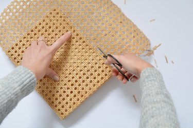 Hands holding cane while cutting with black scissors.