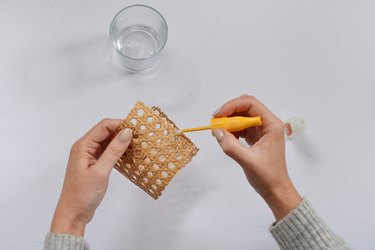 Hand applying glue to cane, glass in background.