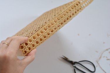 Hand holding cane against wooden lid. Scissors in background.