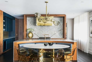 Cut out kitchen island with marble countertop, built-in oval dining booth, white dining table with brass finish base.