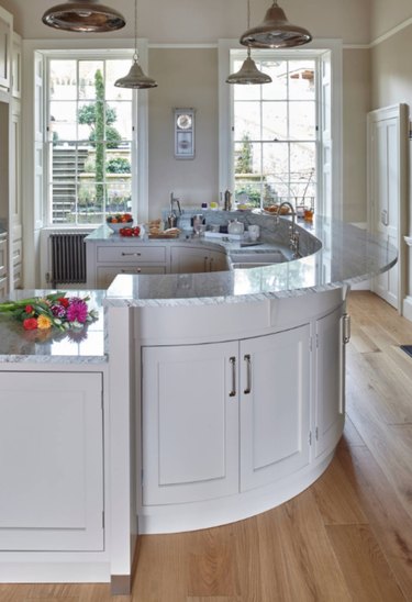 Half oval kitchen island with marble countertop and white cabinets.
