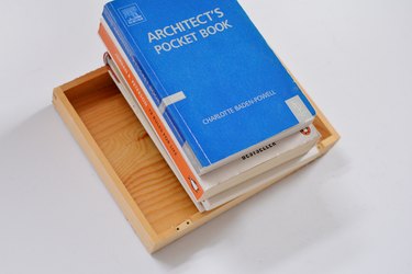 Stack of books weighing down on wooden box lid.