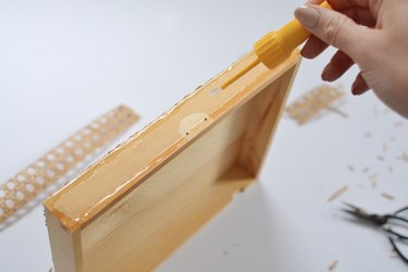 Hand applying glue to wooden box lid.