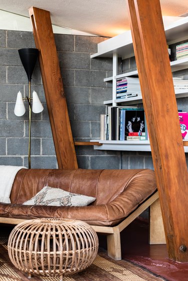 Midcentury home by John Lautner with sloped wooden beams and vintage couch with leather cushion and white wall shelving