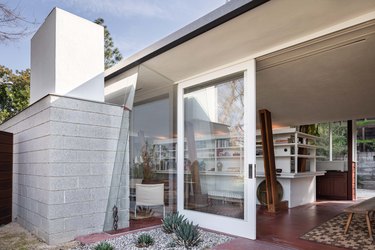 Midcentury home by John Lautner with sloped wooden beams and vintage couch with white bookcases and large glass doors