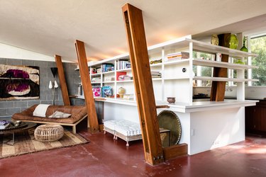 Midcentury home by John Lautner with sloped wooden beams and vintage couch with leather cushion and white wall shelving