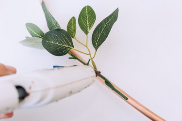 Hot gluing faux greenery to heart wreath