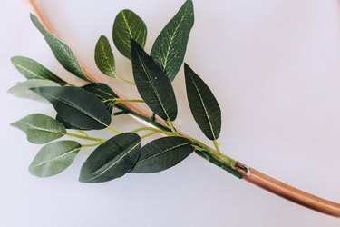 Hot gluing faux greenery to heart wreath