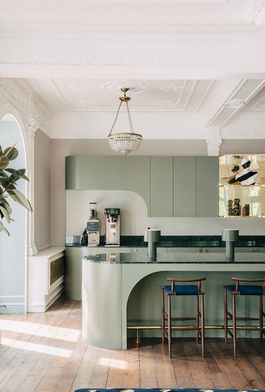 Oval kitchen island in pastel green with bar chaialongside matching cabinets.