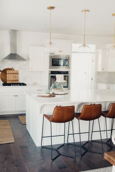 Dark wood kitchen flooring idea with leather bar stools and globe pendant lights