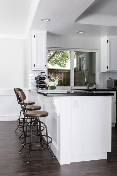 Dark wood kitchen flooring idea with wood and metal bar stools and black countertop