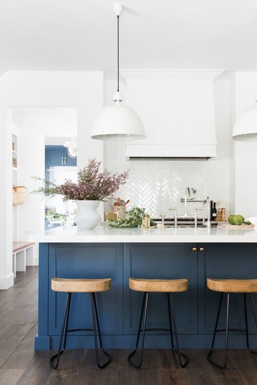 Dark wood kitchen flooring idea with blue island and herringbone white tile backsplash
