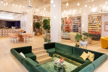 The emerald green conversation pit at the Dumbo, Brooklyn location of The Wing surrounded by rainbow bookshelves