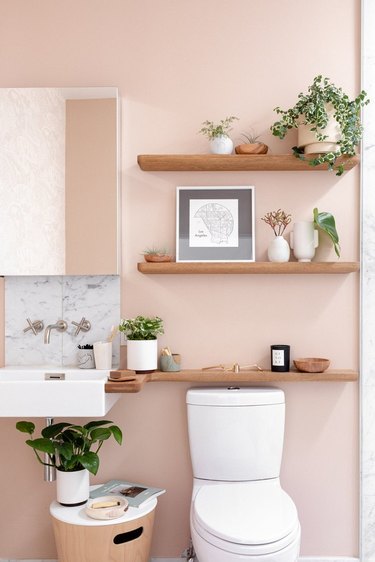 bathroom with millennial pink wall and wood shelves with plants and framed artwork