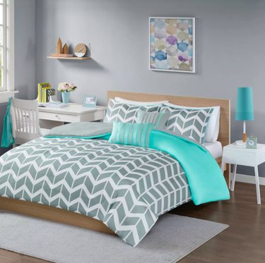 bed with chevron pattern bedding, night stand and desk nearby