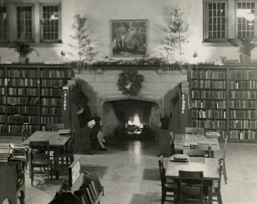 a library featuring an inglenook at Christmas surrounded by two benches and a woman reading a book